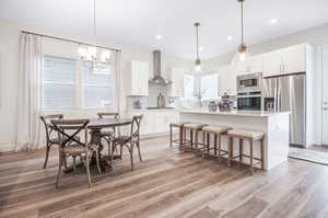 Interior space with white cabinets, appliances with stainless steel finishes, light hardwood / wood-style floors, wall chimney exhaust hood, and tasteful backsplash