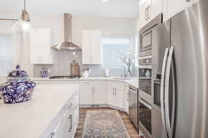 Kitchen featuring white cabinets, backsplash, appliances with stainless steel finishes, wood-type flooring, and wall chimney exhaust hood