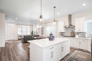 Kitchen with dark wood-type flooring, wall chimney range hood, white cabinets, and tasteful backsplash