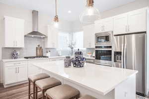 Kitchen with wall chimney range hood, appliances with stainless steel finishes, a kitchen island, and decorative backsplash