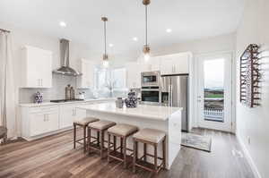 Kitchen with hardwood / wood-style flooring, a center island, appliances with stainless steel finishes, wall chimney range hood, and decorative backsplash