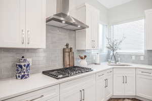 Kitchen featuring wall chimney exhaust hood, stainless steel gas stovetop, sink, decorative backsplash, and hardwood / wood-style flooring