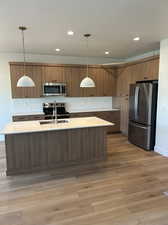 Kitchen featuring a kitchen island with sink, decorative light fixtures, appliances with stainless steel finishes, and light hardwood / wood-style floors