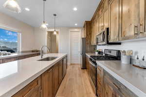 Kitchen featuring light stone counters, stainless steel appliances, light hardwood / wood-style floors, sink, and pendant lighting