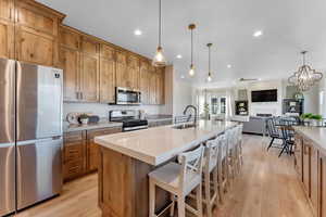 Kitchen featuring light wood-type flooring, appliances with stainless steel finishes, sink, an island with sink, and pendant lighting