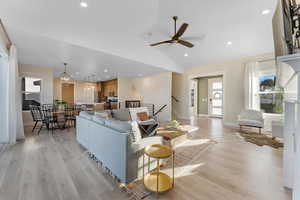 Living room featuring vaulted ceiling, ceiling fan with notable chandelier, and light hardwood / wood-style floors