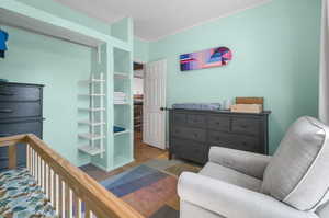 Bedroom with hardwood / wood-style floors, a nursery area, and crown molding