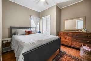 Bedroom with ceiling fan, ornamental molding, a closet, and dark hardwood / wood-style flooring