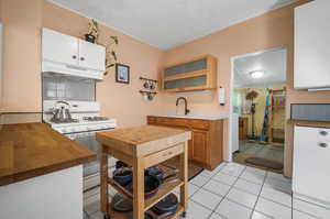 Kitchen with white range with gas cooktop, a textured ceiling, light tile patterned floors, sink, and decorative backsplash