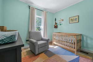 Bedroom with hardwood / wood-style floors, a nursery area, and crown molding