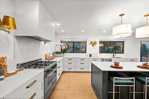 Kitchen with white cabinets, stainless steel appliances, light hardwood / wood-style floors, sink, and pendant lighting