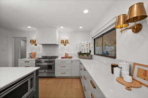 Kitchen with appliances with stainless steel finishes, light stone counters, custom exhaust hood, and light hardwood / wood-style floors