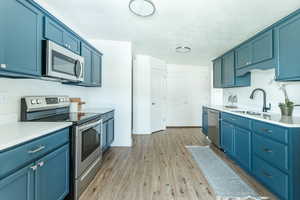 Kitchen with blue cabinets, appliances with stainless steel finishes, sink, and light hardwood / wood-style floors