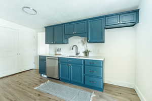 Kitchen featuring stainless steel dishwasher, sink, light hardwood / wood-style flooring, and blue cabinetry