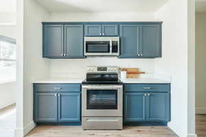 Kitchen with light wood-type flooring, appliances with stainless steel finishes, and blue cabinetry