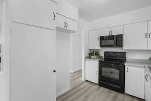 Kitchen featuring black appliances, white cabinetry, and light vinyl  wood-style flooring