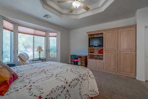 Bedroom with carpet flooring, ceiling fan, and a raised ceiling