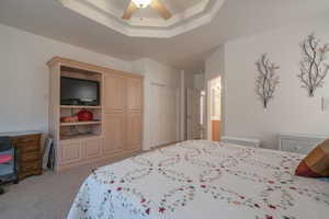 Bedroom with ceiling fan, light carpet, and a tray ceiling