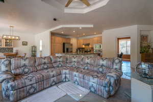 Living room with ceiling fan with notable chandelier, a raised ceiling, and light tile patterned floors