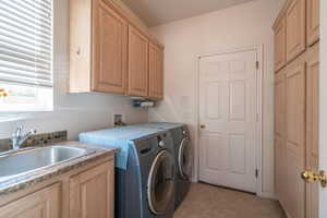 Clothes washing area featuring cabinets, light tile patterned floors, washer and clothes dryer, and sink