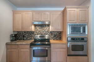 Kitchen with backsplash, light brown cabinets, and stainless steel appliances