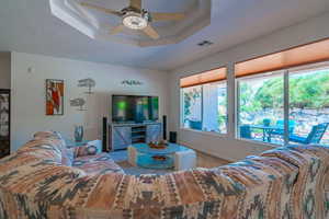 Living room with carpet flooring, ceiling fan, and a tray ceiling