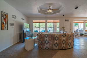 Tiled living room featuring a textured ceiling, a raised ceiling, and ceiling fan