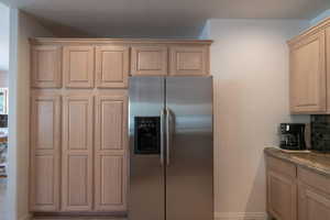 Kitchen featuring dark stone counters, light brown cabinets, decorative backsplash, and stainless steel fridge with ice dispenser