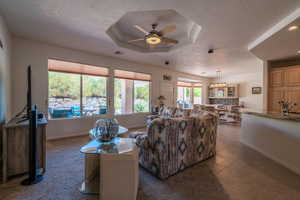 Tiled living room with a raised ceiling, a textured ceiling, and ceiling fan