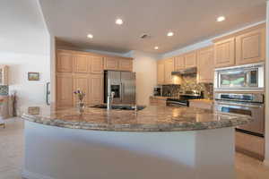 Kitchen featuring light tile patterned floors, stainless steel appliances, sink, light brown cabinets, and decorative backsplash