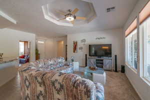 Living room with a tray ceiling, ceiling fan, and carpet