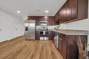 Kitchen featuring appliances with stainless steel finishes, light stone countertops, sink, and light hardwood / wood-style flooring