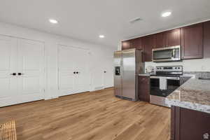 Kitchen featuring appliances with stainless steel finishes, light stone counters, and light hardwood / wood-style floors