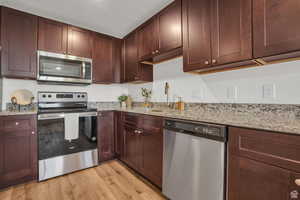 Kitchen with sink, light stone countertops, appliances with stainless steel finishes, and light hardwood / wood-style floors