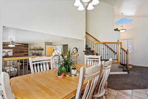 Dining area featuring carpet flooring, ceiling fan with notable chandelier, and high vaulted ceiling