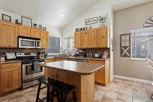 Kitchen featuring backsplash, light tile patterned floors, a center island, sink, and appliances with stainless steel finishes