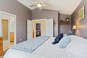 Bedroom with ceiling fan, vaulted ceiling, ensuite bath, and light tile patterned flooring