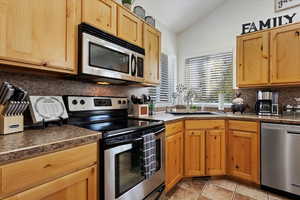 Kitchen with vaulted ceiling, light tile patterned floors, appliances with stainless steel finishes, tasteful backsplash, and sink