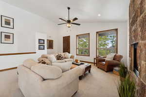 Living room with ceiling fan, a fireplace, vaulted ceiling, and light colored carpet