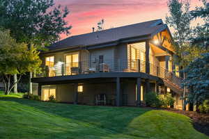 Back house at dusk featuring a lawn and a balcony