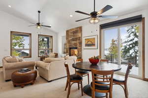 Carpeted dining space with ceiling fan, a fireplace, and vaulted ceiling