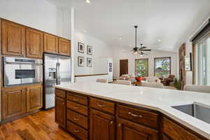 Kitchen with lofted ceiling, ceiling fan, light stone countertops, light hardwood / wood-style floors, and stainless steel appliances