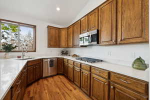 Kitchen with lofted ceiling, sink, appliances with stainless steel finishes, and light hardwood / wood-style floors