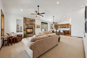 Living room with vaulted ceiling, a fireplace, light colored carpet, and ceiling fan