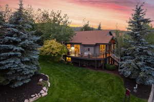 Back house at dusk featuring a lawn and a wooden deck