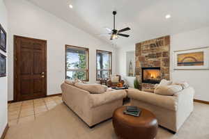 Tiled living room featuring a stone fireplace, ceiling fan, and vaulted ceiling