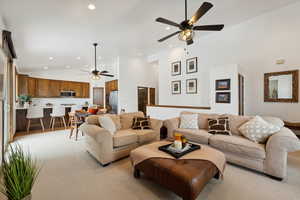 Carpeted living room featuring ceiling fan and high vaulted ceiling