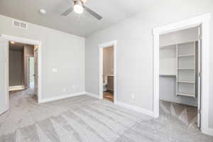 Unfurnished bedroom featuring a spacious closet, ceiling fan, light carpet, ensuite bath, and a closet