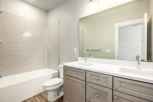 Full bathroom with hardwood / wood-style flooring, vanity, tiled shower / bath, and toilet