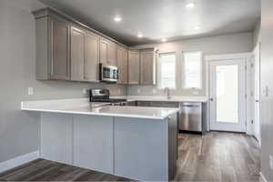 Kitchen with sink, dark wood-type flooring, kitchen peninsula, and appliances with stainless steel finishes